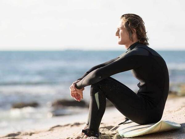 A young surfer sitting on the beach represents the full life that can be led after testicular cancer treatment.