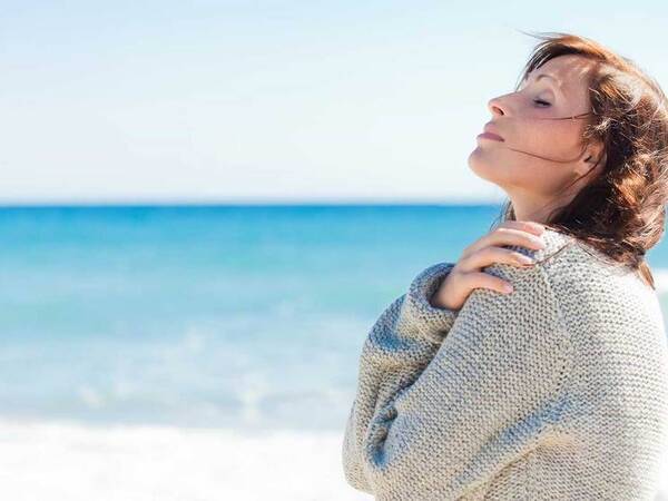 A calm middle-aged woman at the beach represents the full life that can be led after urethral cancer treatment.