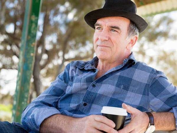 A smiling middle-aged man drinking coffee in a park represents the full life that can be led after parathyroid cancer treatment.