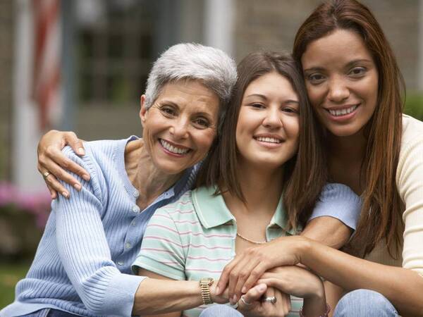 Multi-generational family of women smiling outside their family home, representing different stages of life and OB-GYN services.